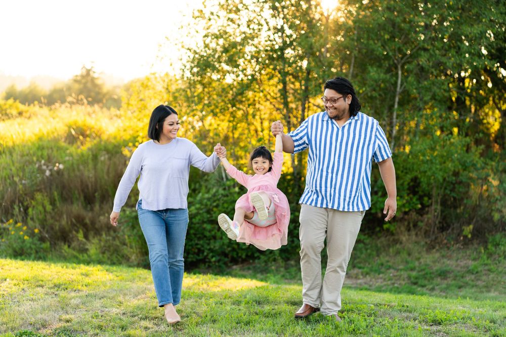 Parents swinging their daughter at sunset in Marymoor Park.