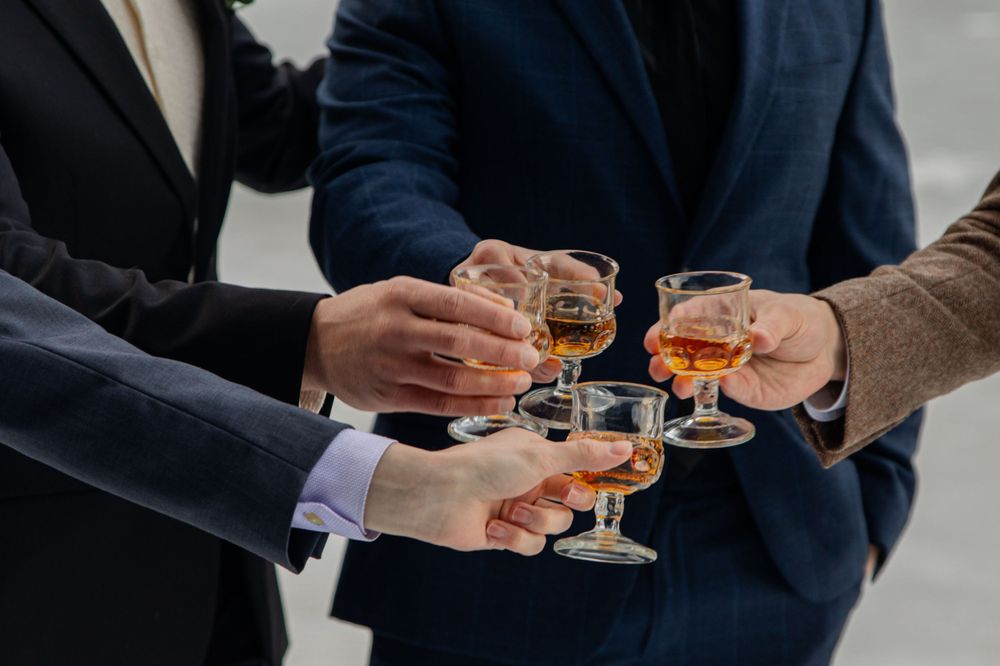 Three people in formal attire toast with glasses of whiskey during a celebration.