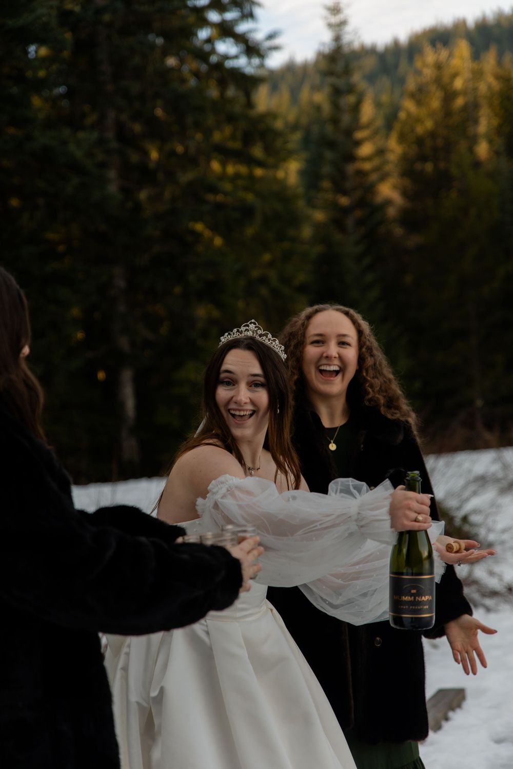 A winter wedding celebration with laughter and champagne in a snowy forest setting.