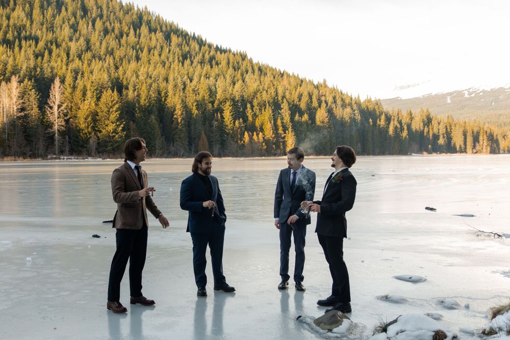 Four people stand on a frozen lake with tree-filled mountains in the background.