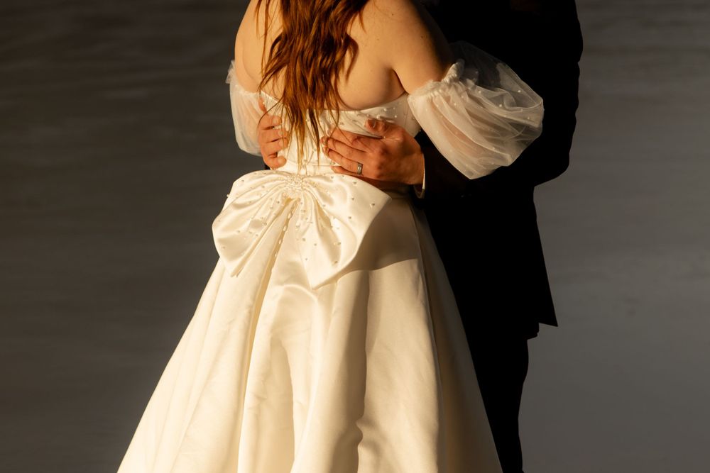 Close up of formal wedding attire showing a white dress with bow detail and black suit.