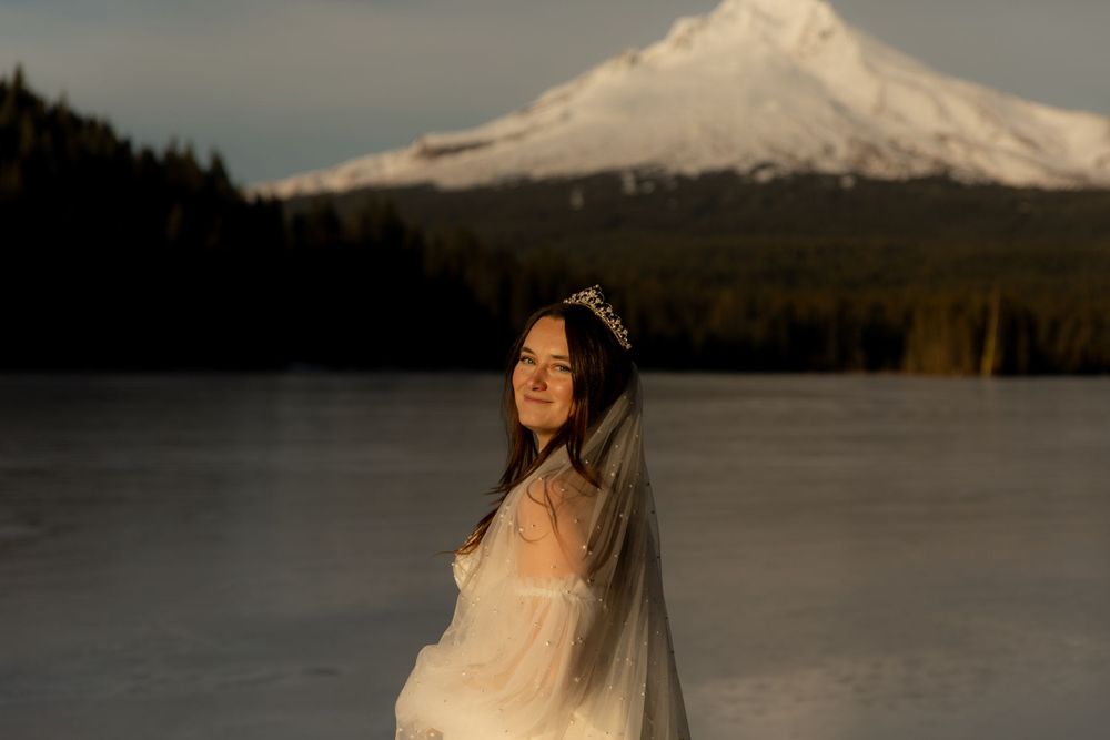 A stunning winter wedding portrait with Mount Hood rising in the background over a frozen lake.