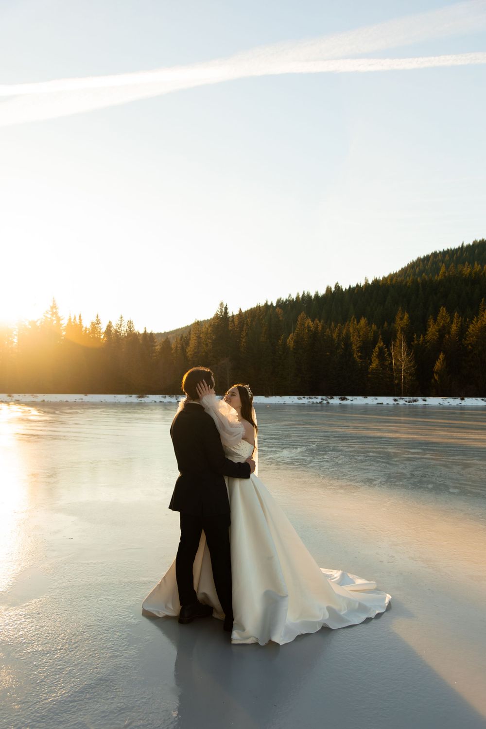 Couple shares intimate moment on frozen lake during sunset with mountain backdrop.