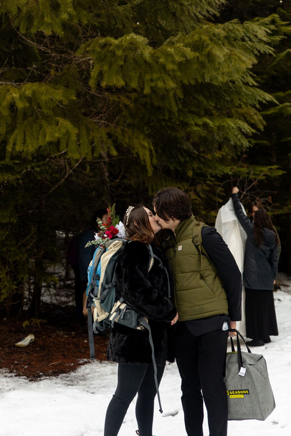 Winter wedding scene with couple sharing intimate moment among snow-covered evergreens.