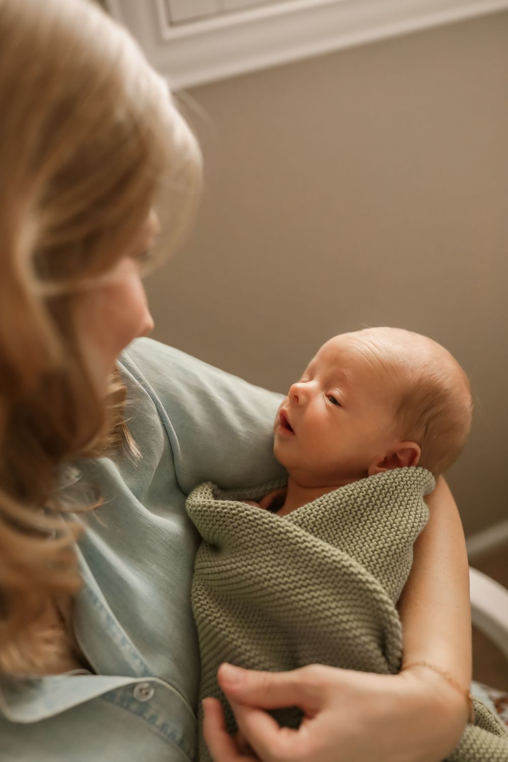 A mother tenderly holds her sleeping newborn baby wrapped in a soft green knit blanket.