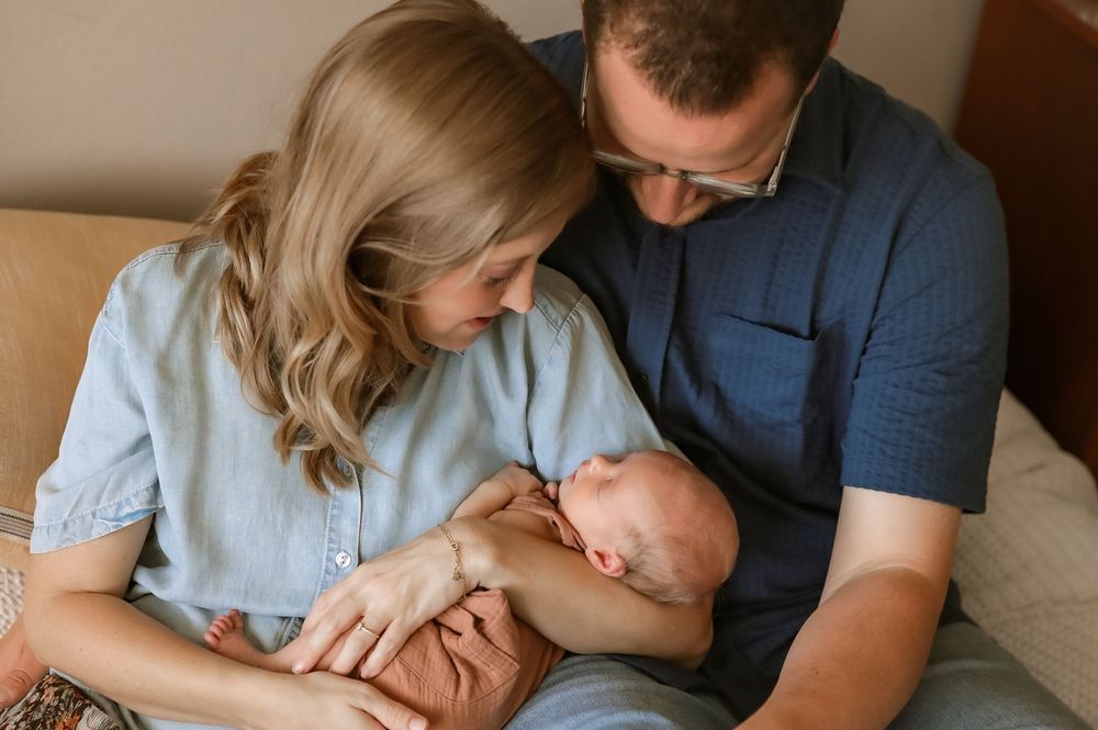 New parents tenderly gaze at their sleeping newborn baby during an intimate family portrait session.