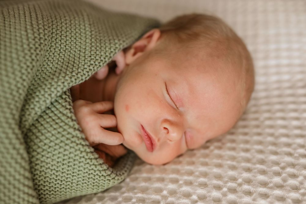 Peaceful newborn baby sleeping wrapped in a soft green knit blanket, perfect newborn photography portrait.