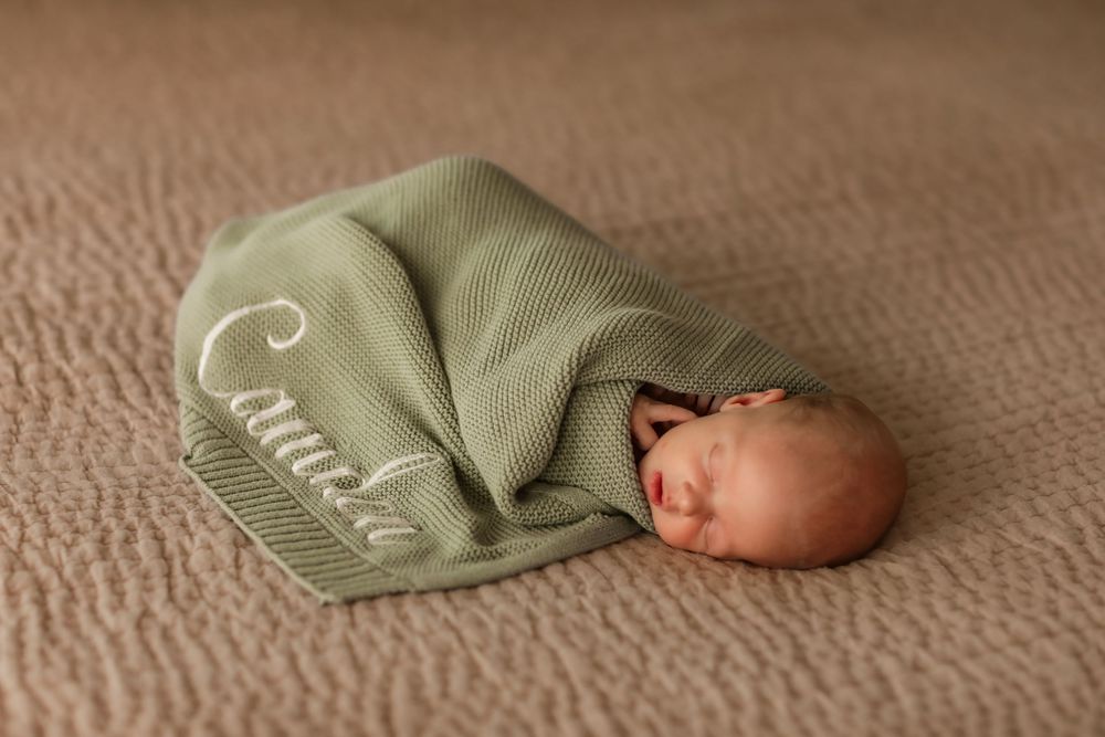 Newborn baby named Caurie sleeps peacefully swaddled in a personalized green knit blanket.