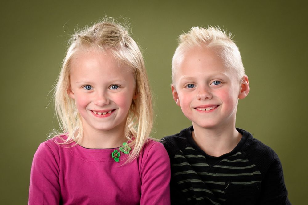Two children posing together against a green background.