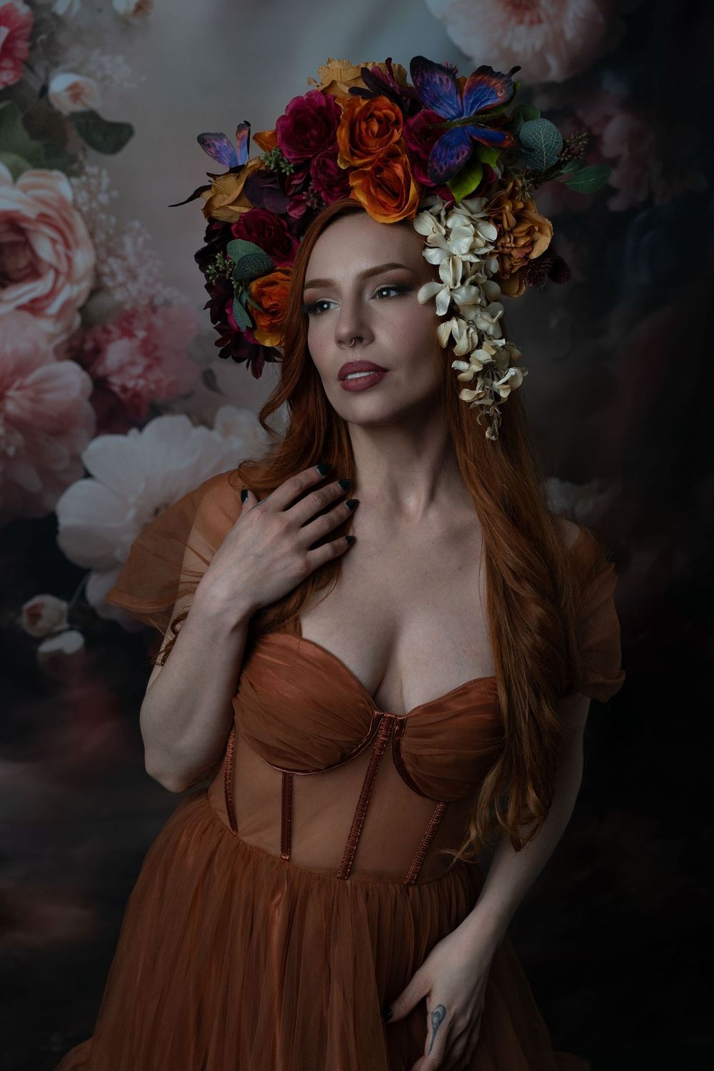 A woman in a rust tulle gown wears a vibrant floral crown, posing against a soft floral backdrop.