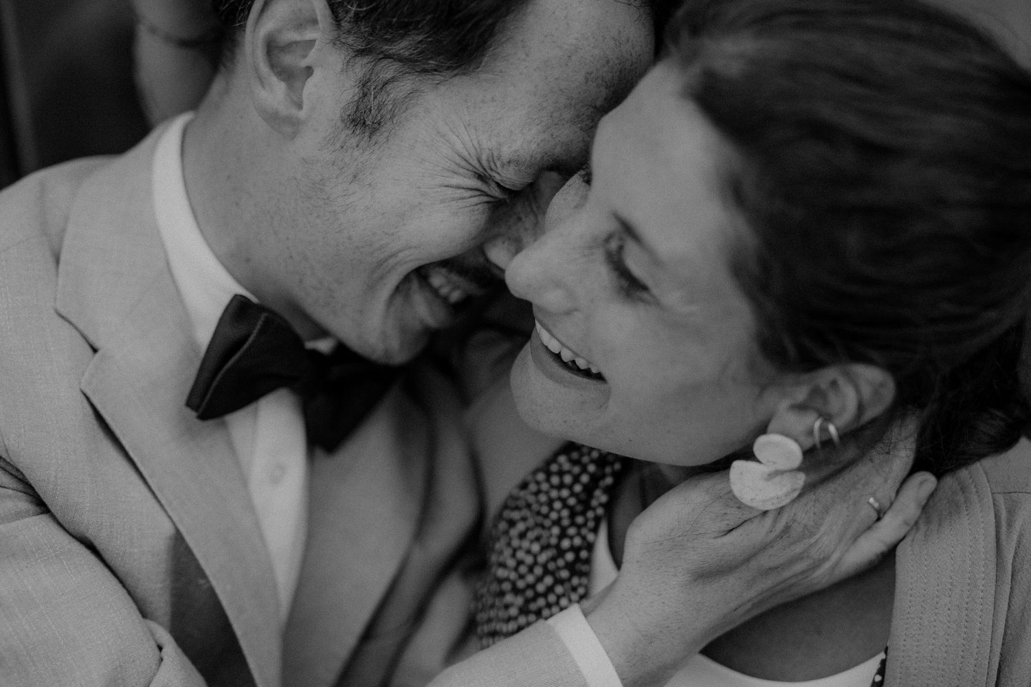 Black and white photo of a laughing bride and groom touching foreheads on their wedding day.