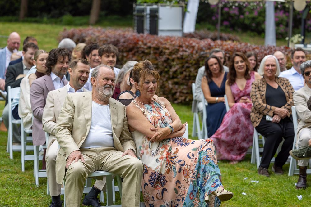 Gasten kijken lachend en trots naar bruidspaar tijdens de ceremonie - bruidsreportage aan huis - Teteringen in eigen achtertuin - MaxFotos