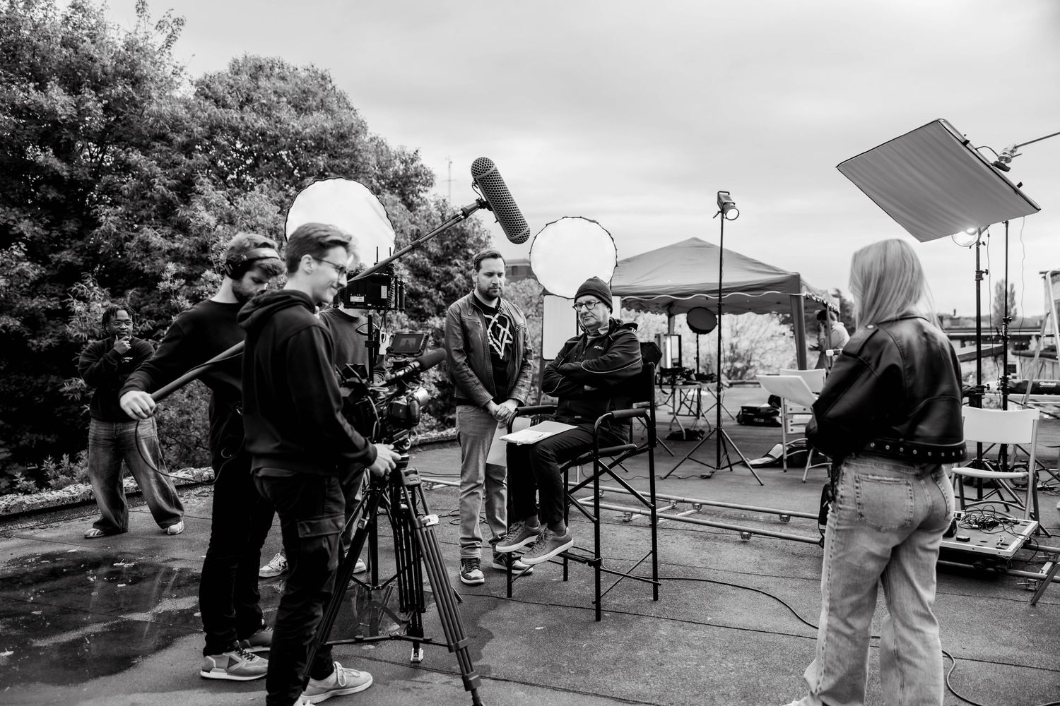 Two videographers in black hoodies filming on a cloudy beach with professional cameras and backpacks.