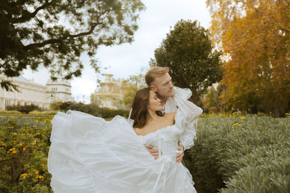 Couple sharing a romantic kiss in lush garden, bride in flowing white dress, autumn backdrop.