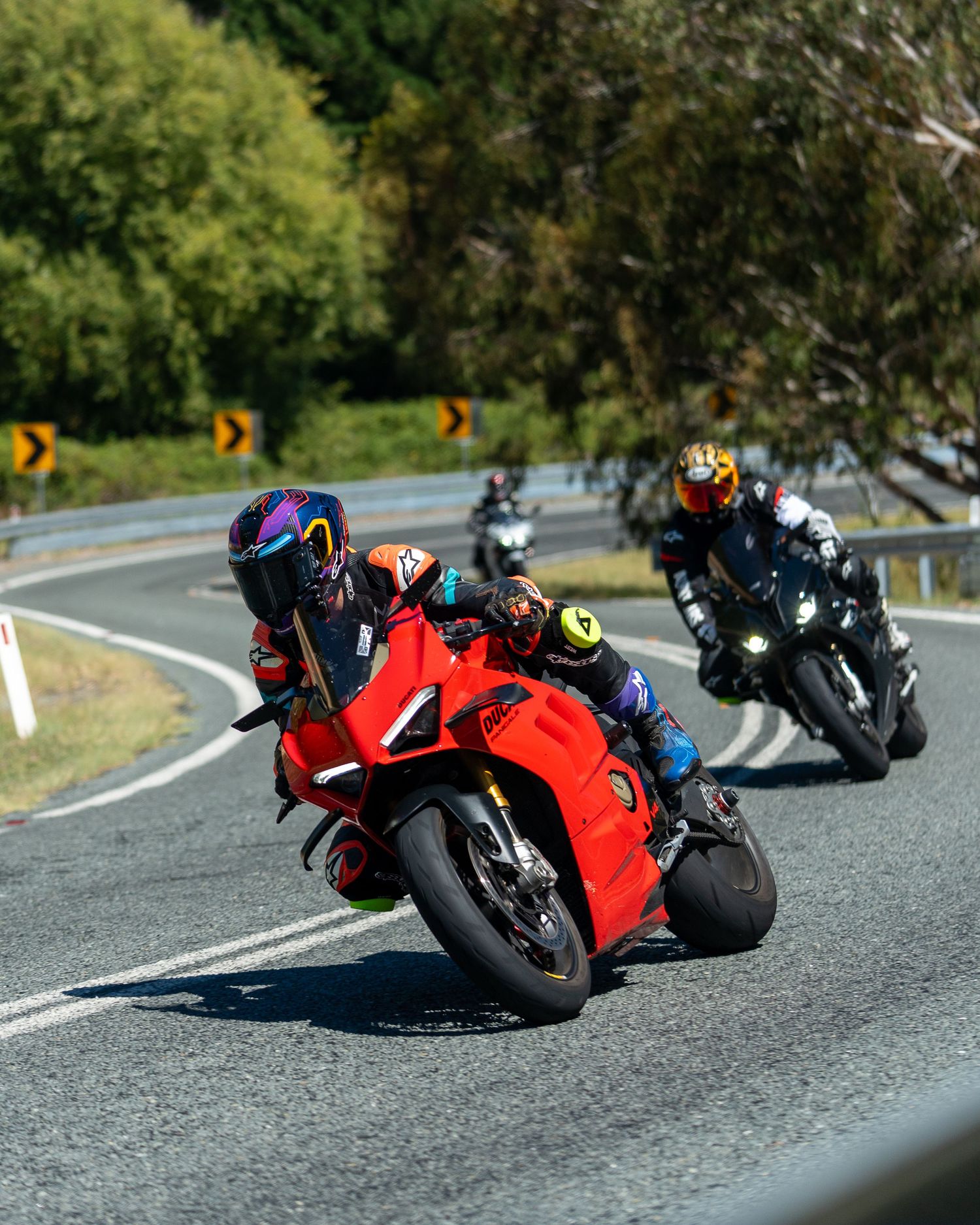 Two riders on red Ducati motorcycles cornering on a scenic winding road.