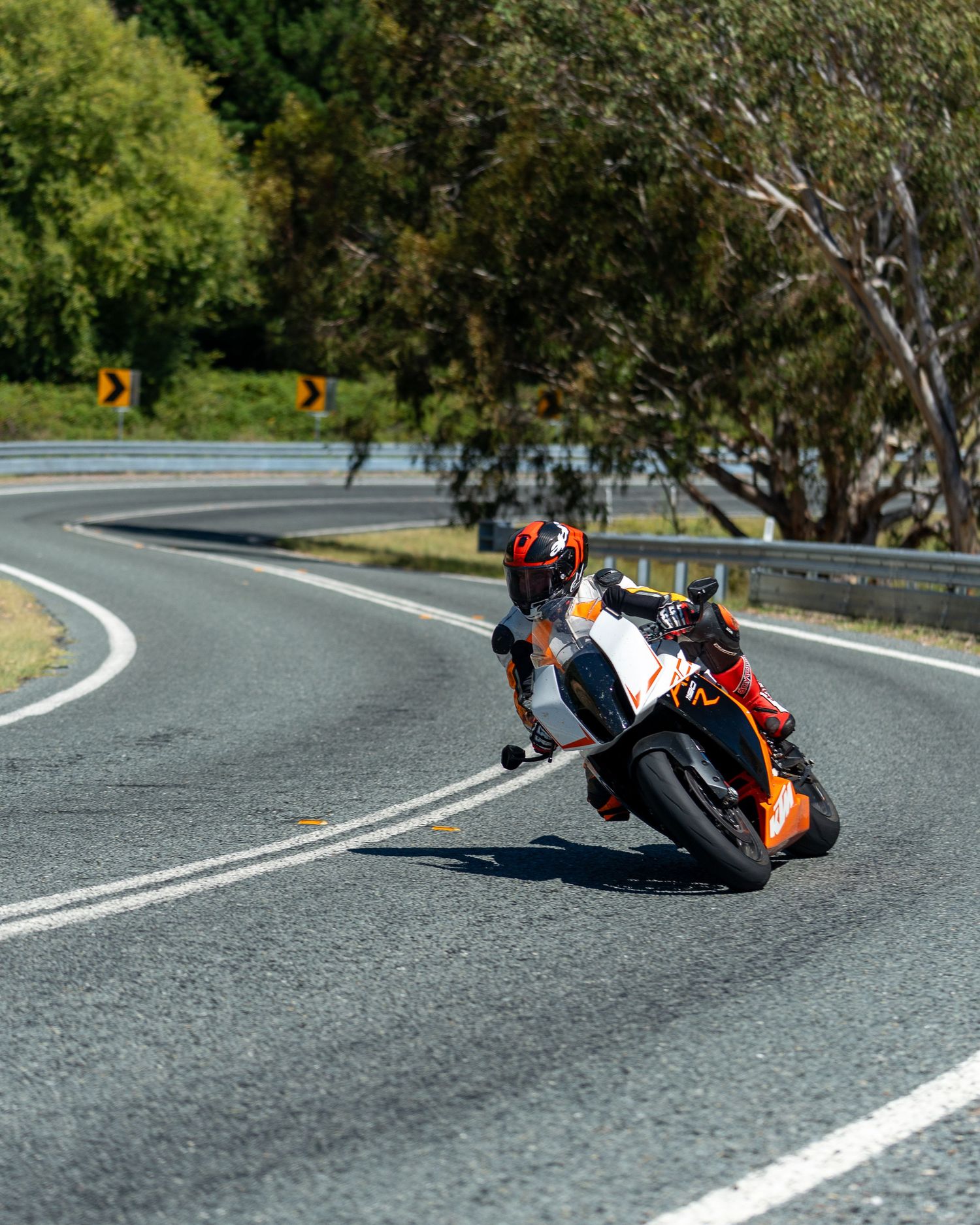 Rider aggressively cornering an orange KTM RC sports motorcycle on a sunny road.