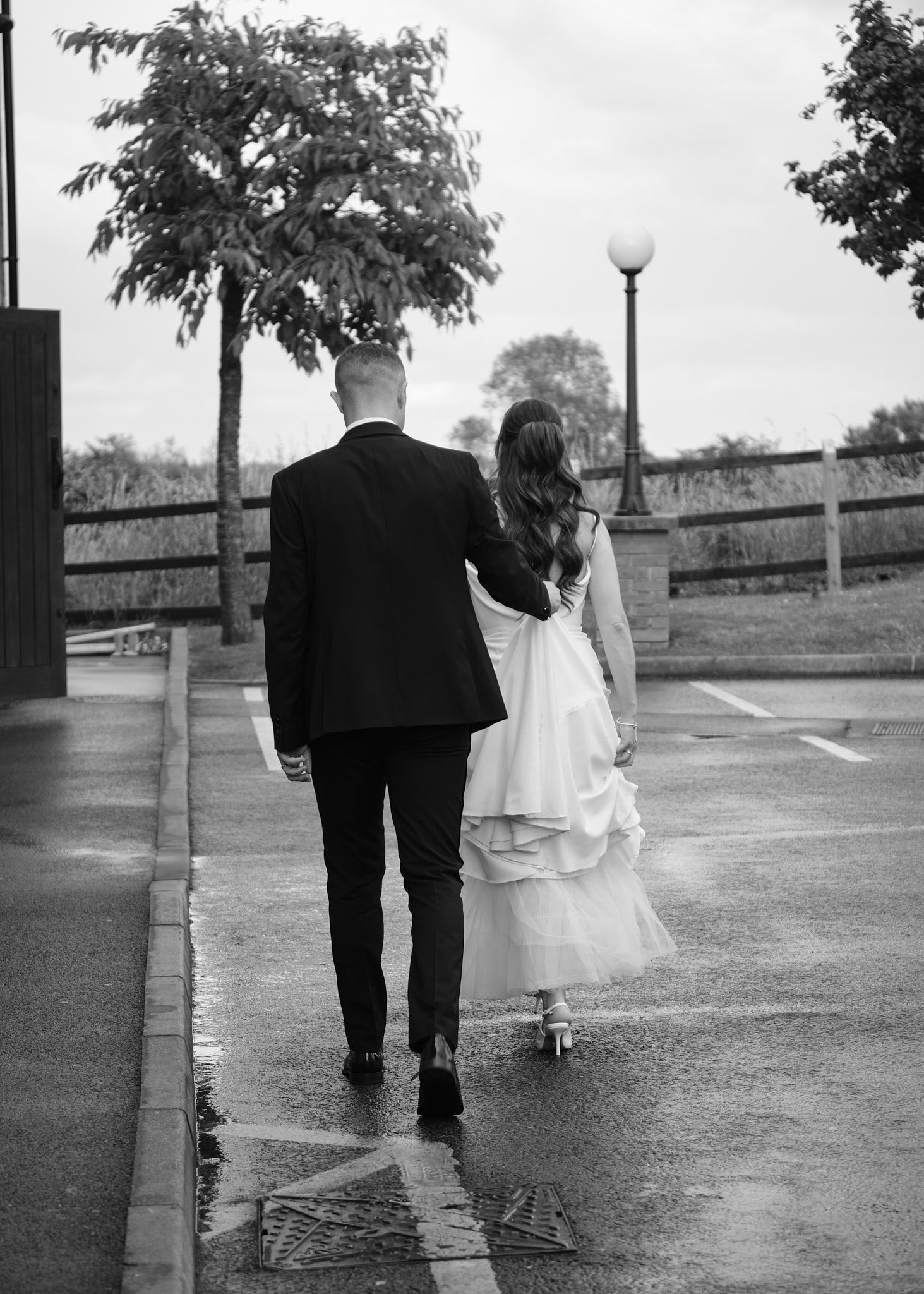 Black and white photo of newlywed couple walking away together in rain after wedding.