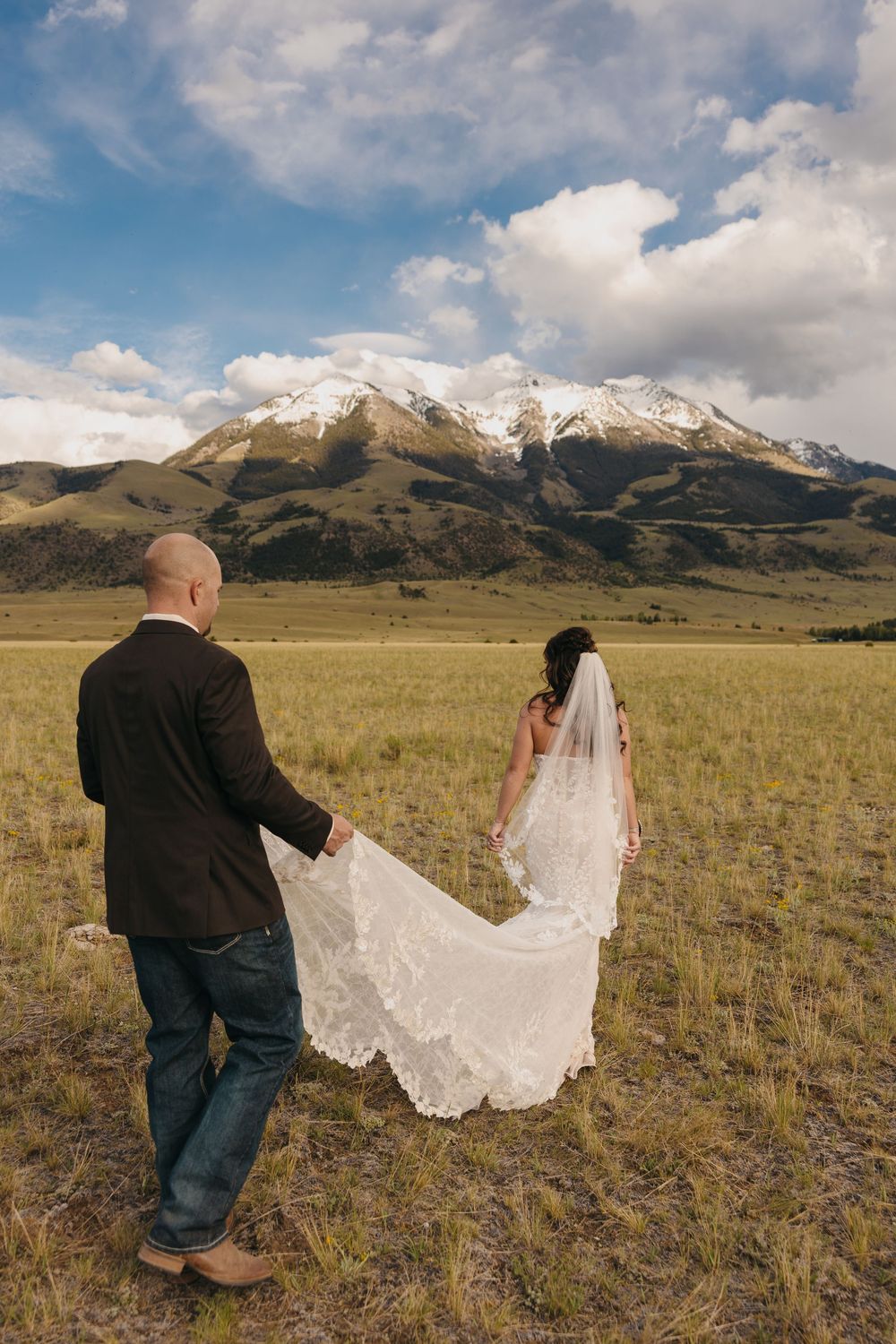 Paradise Valley Groom holds brides dress under the Mountains in Chico, Montana captured by Pray Montana Elopement Photographer Sabrina Marie