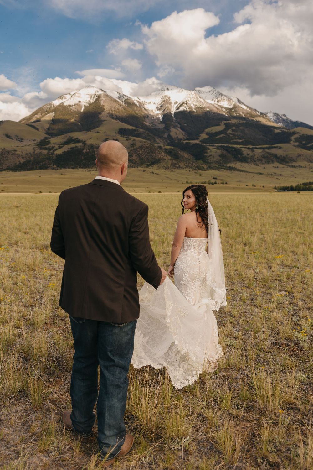 Paradise Valley Groom holds brides dress under the Mountains in Chico, Montana captured by Pray Montana Elopement Photographer Sabrina Marie