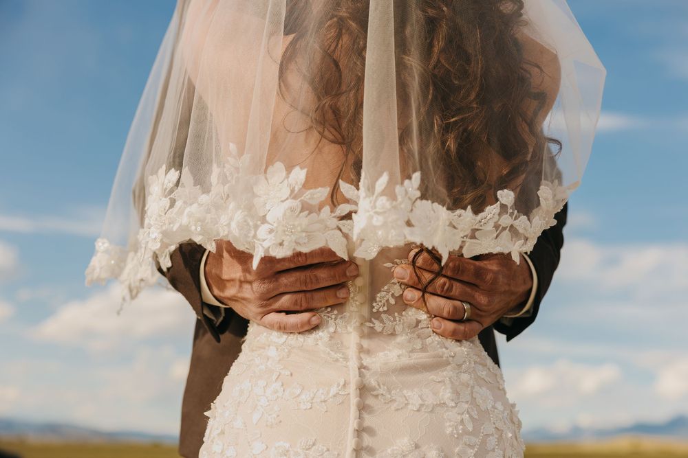 Paradise Valley Groom holds brides dress under the Mountains in Chico, Montana captured by Pray Montana Elopement Photographer Sabrina Marie