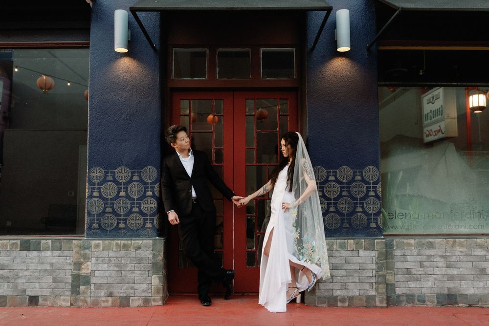 Bride and groom holding hands outside a blue building with red doors in Chinatown.