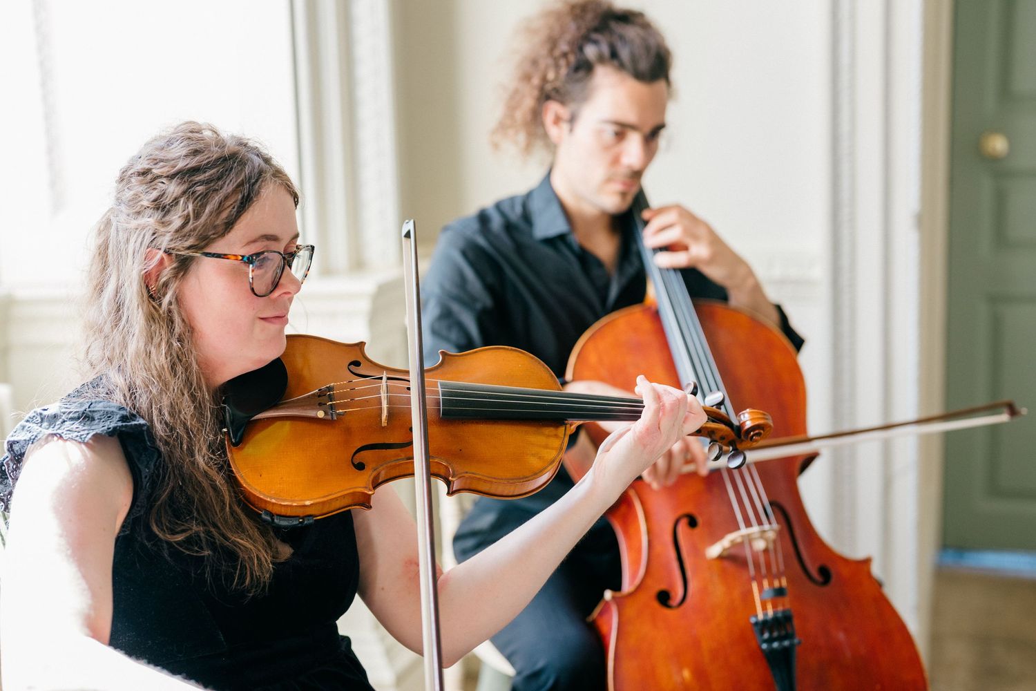 Two musicians playing violin and cello together in a bright room during a classical music performance.