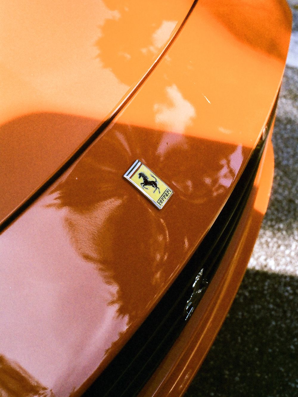 Close-up of an orange Ferrari sports car featuring the iconic prancing horse badge on the rear trunk lid.