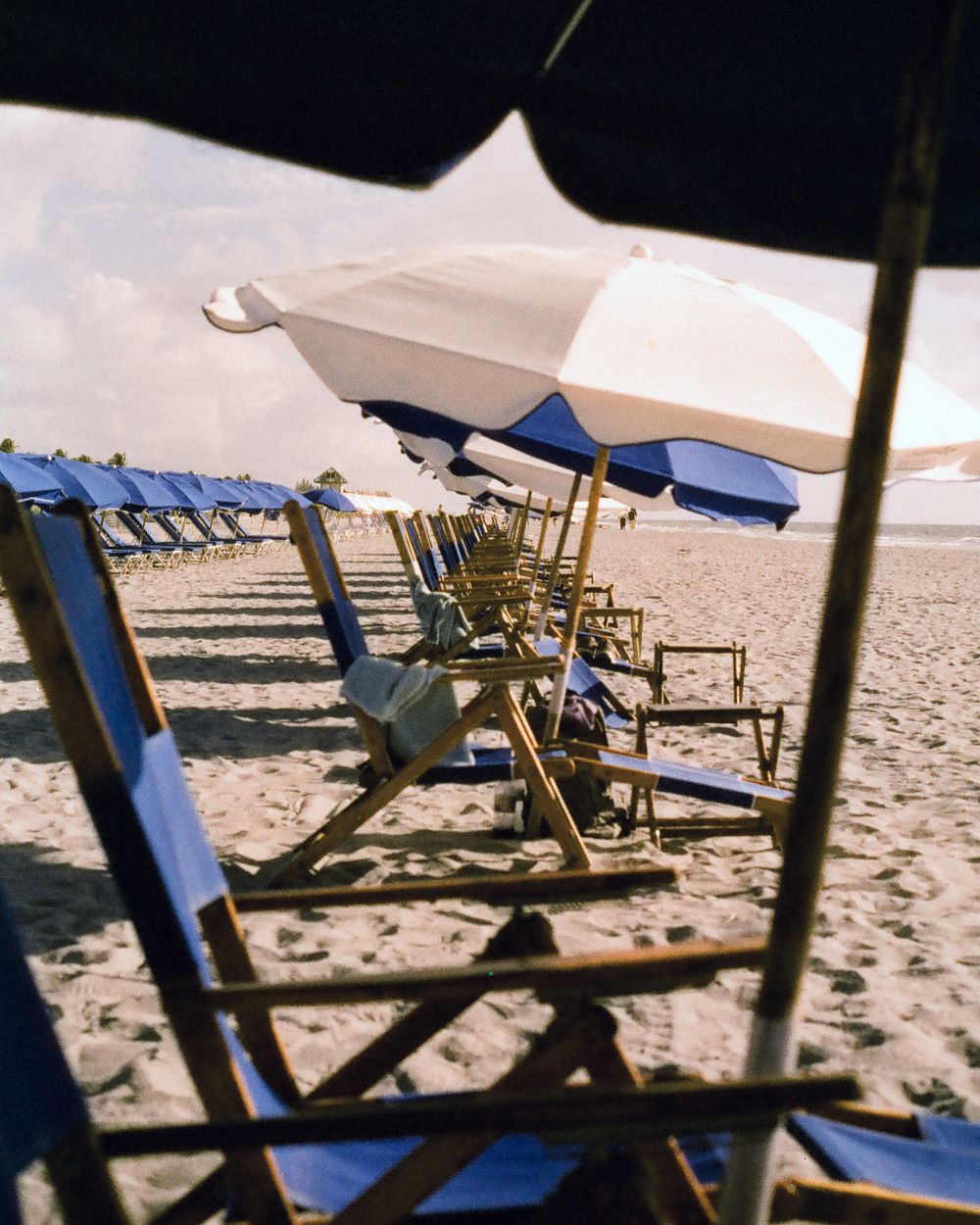 Rows of wooden beach chairs and blue-white striped umbrellas lined up on a sandy beach resort.