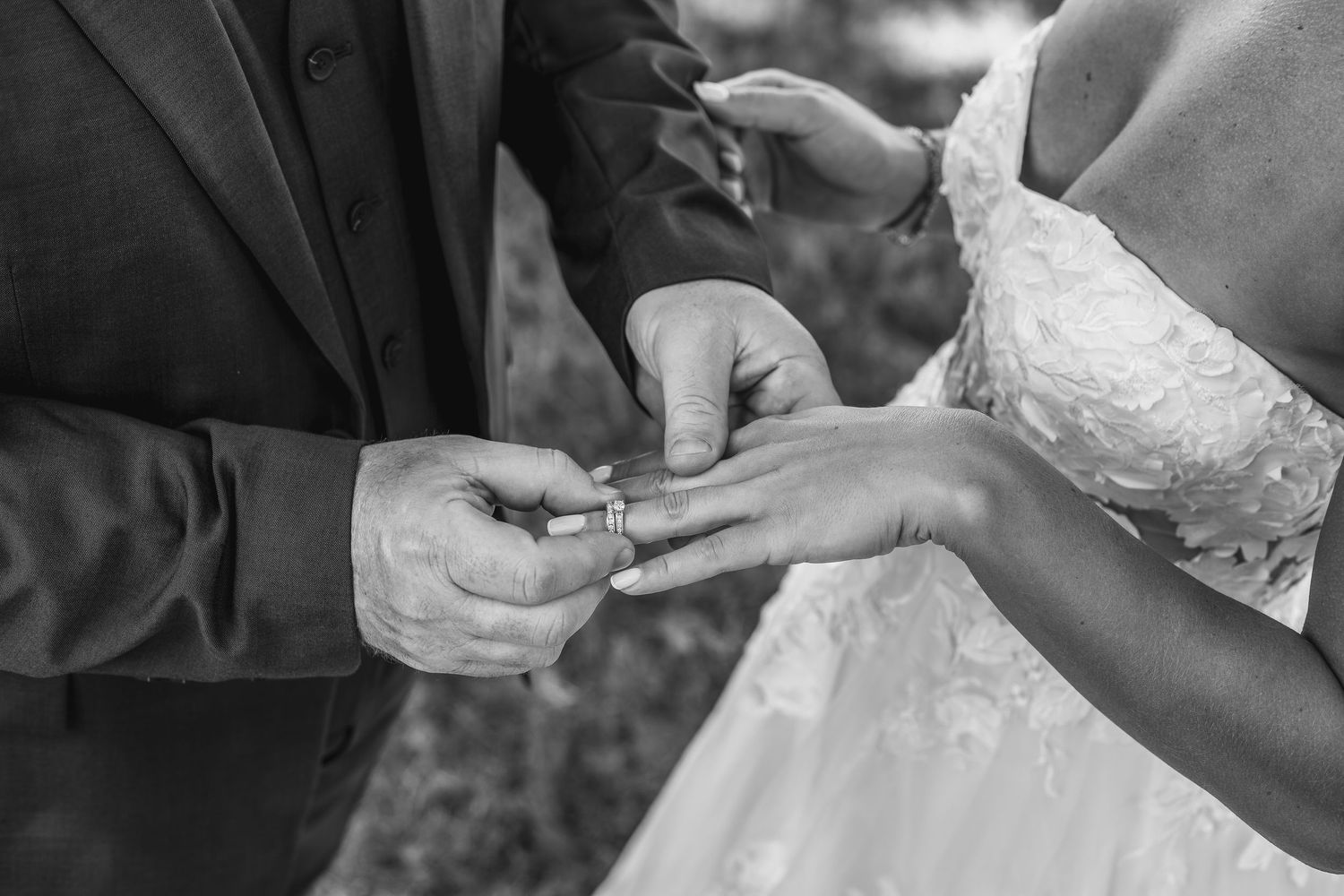 Black and white photo of groom placing wedding ring on bride's finger during ceremony.