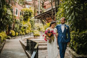 Wedding couple walks along lush garden path with vintage architecture.