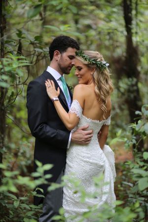 Romantic forest wedding portrait with couple embracing among lush greenery.