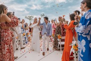 Wedding party and guests celebrating on a beach with colorful attire.