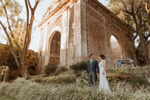 Wedding couple standing by ancient stone ruins in warm sunset light.