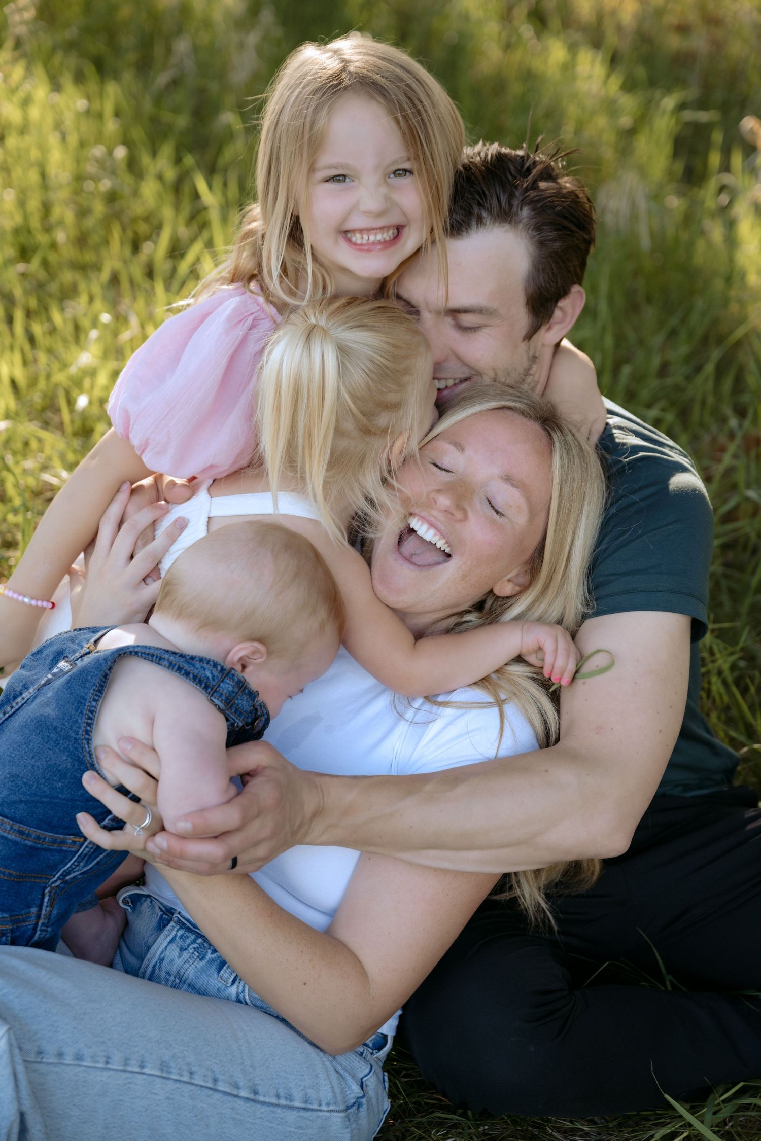 three toddlers tackle mom and dad during a lifestyle outdoor spring family session in Hudson, WI