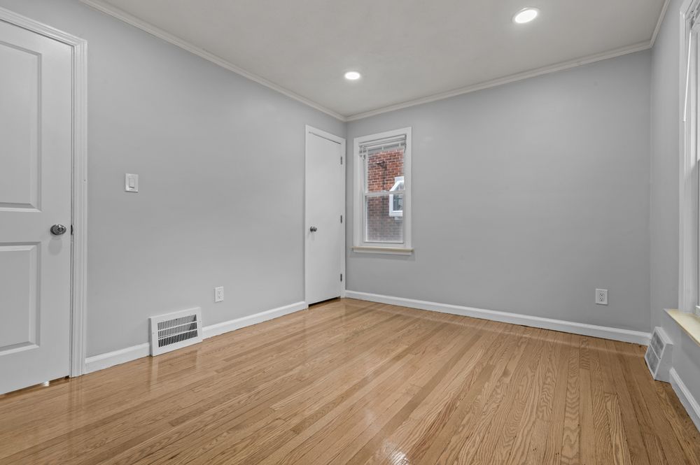Bright empty room with light hardwood floors, white walls, crown molding, recessed lighting, and a window letting in natural light.