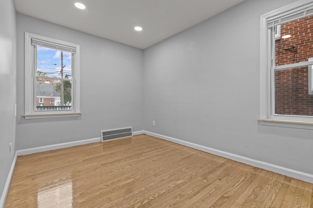 Bright empty room with hardwood floors, recessed lighting, baseboard heater, and two windows.