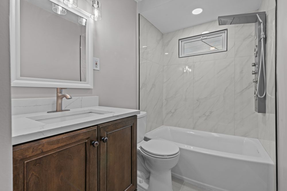 Modern bathroom with dark wood vanity, white marble shower surround, soaking tub, and toilet.