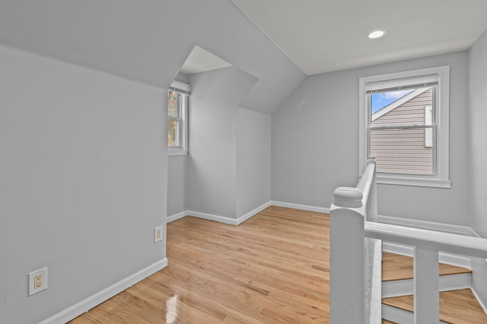 Bright attic bedroom with vaulted ceiling, hardwood floors, and natural light from two windows.