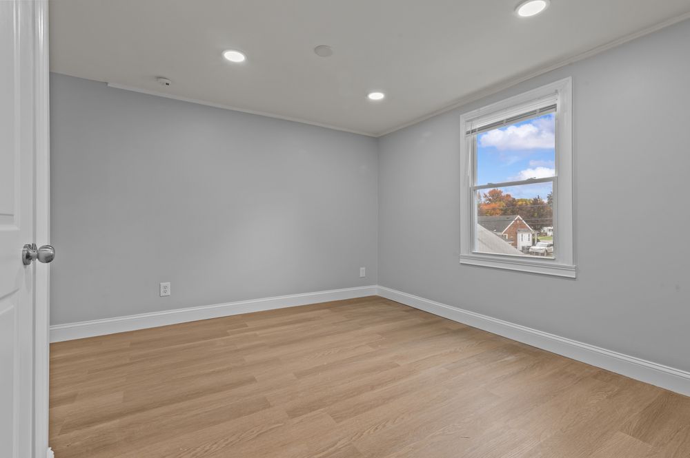 Empty room with light gray walls, hardwood floors, recessed lighting, and a window with natural light.