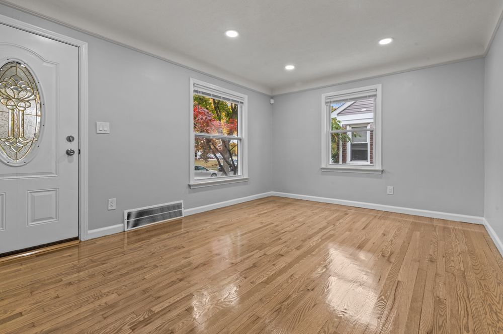 Bright empty living room with hardwood floors, recessed lighting, crown molding, and oval glass front door.