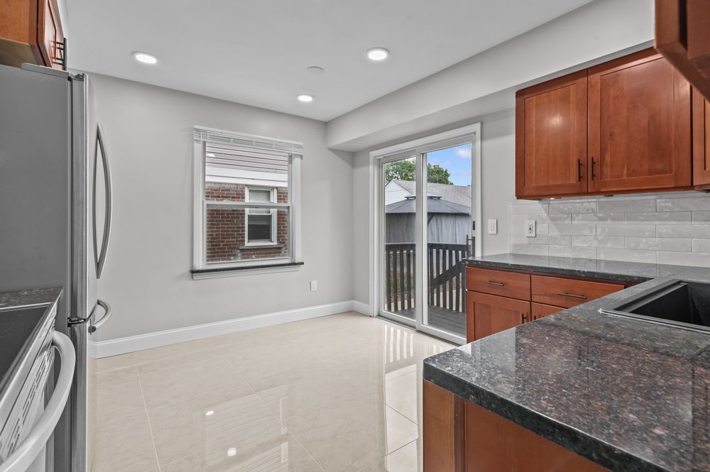 Modern kitchen with cherry wood cabinets, granite countertops, stainless steel fridge, and sliding glass door to balcony.