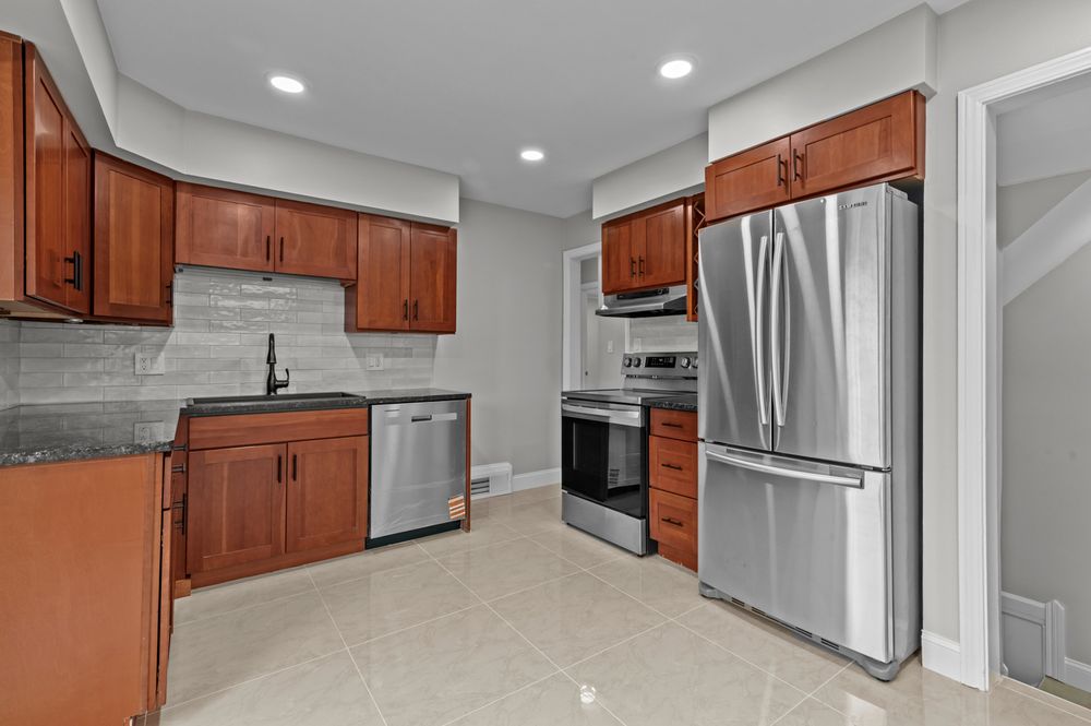 Modern kitchen with cherry wood cabinets, stainless steel appliances, gray backsplash, and light tile flooring.