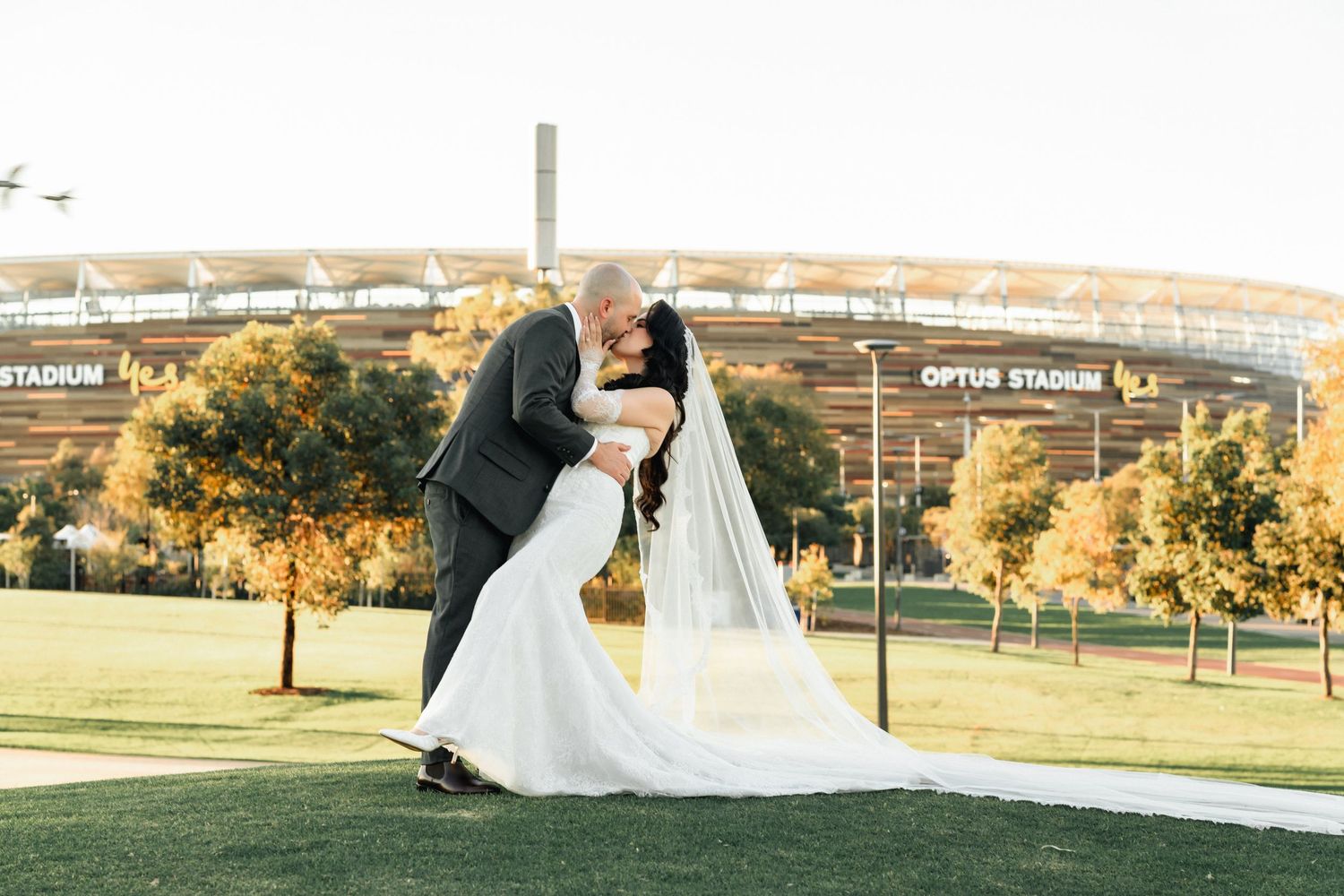 Bride and groom share romantic dip kiss in front of Optus Stadium Perth on their wedding day.