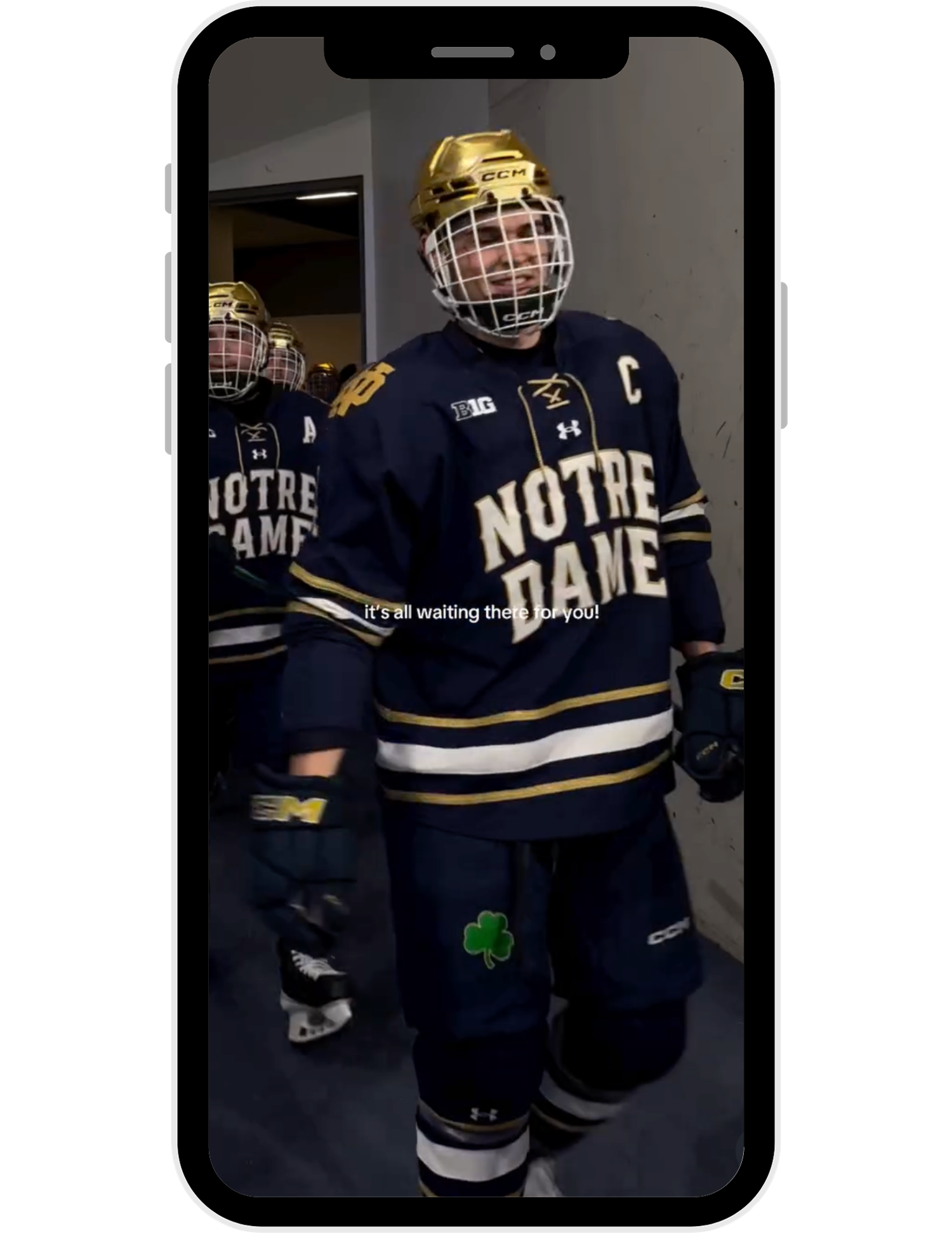 Notre Dame hockey player in navy jersey with captain C patch walks through tunnel in full gear and helmet.