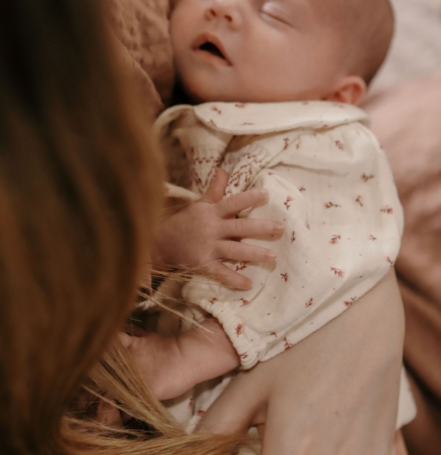 A newborn baby in a floral onesie rests peacefully in a mother's arms.
