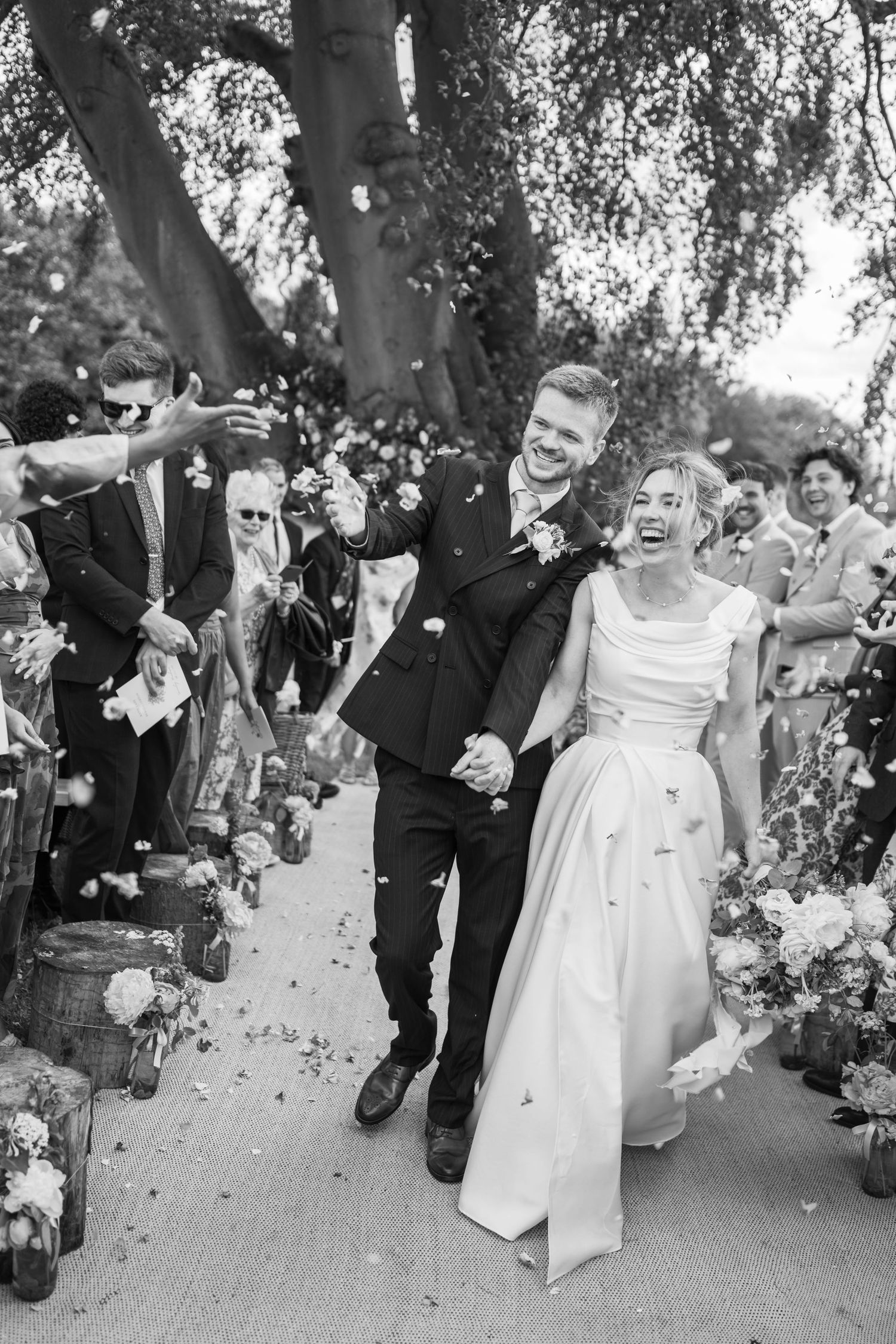 Black and white photo of a joyful bride and groom walking down the aisle as guests throw confetti at their wedding.
