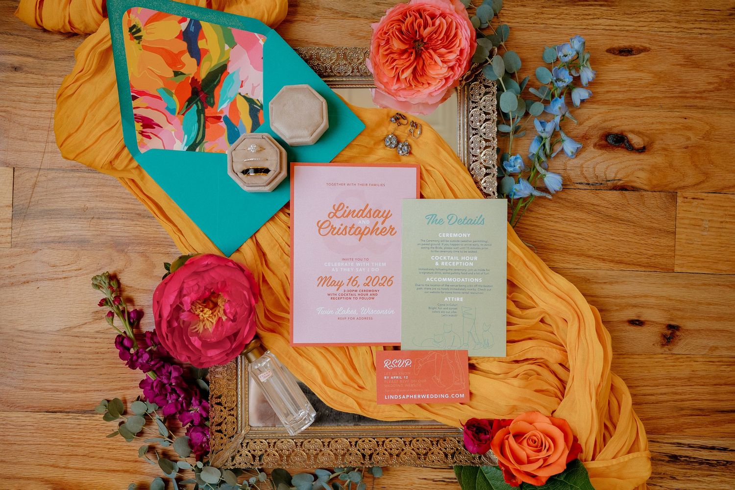 Colorful wedding stationery flat lay with pink, green, and orange invitations, teal envelope, and vibrant floral accents on gold tray.
