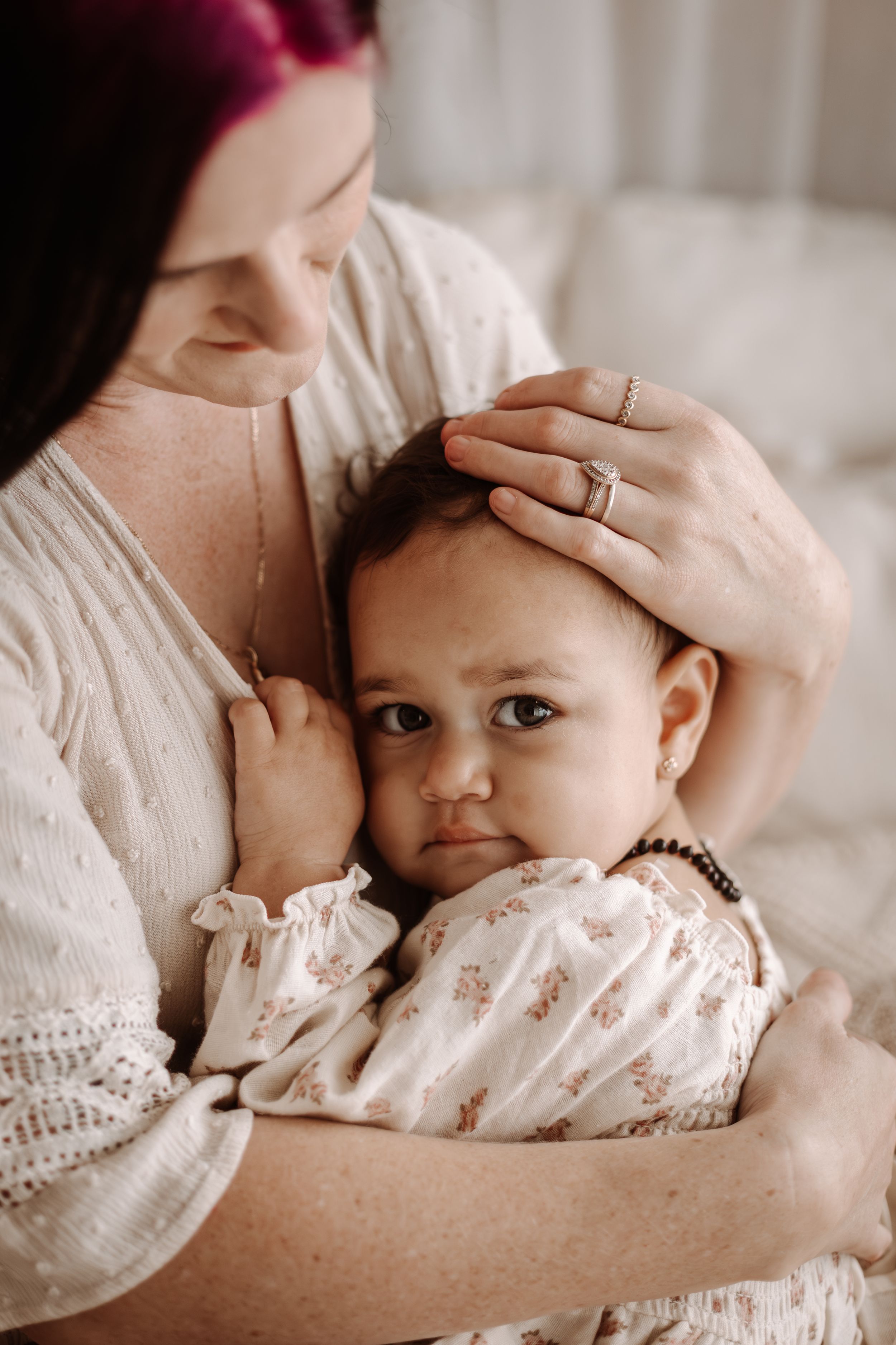 Mother tenderly holds baby against her chest while gently stroking infant's dark hair indoors.