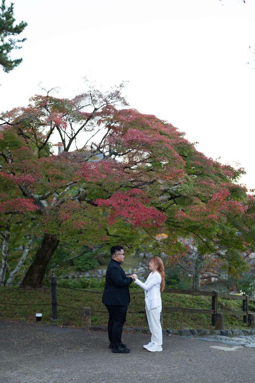 Couple holding hands facing each other under stunning red maple tree in Japanese garden.