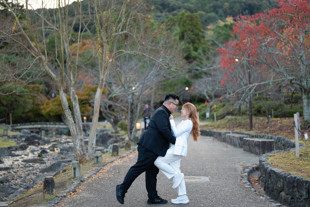 Couple sharing a romantic dip kiss on a scenic autumn park pathway in Japan.